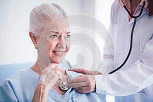 Happy Elderly patient talk with woman doctor at room in hospital. Doctor use stethoscope listening lung of elderly patient.