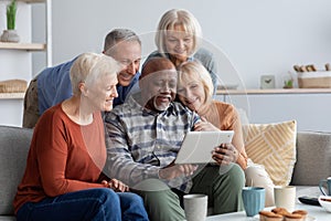 Happy elderly people spending time together at home, using gadgets