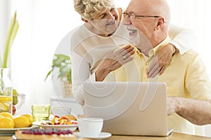 Happy elderly people using laptop while eating breakfast