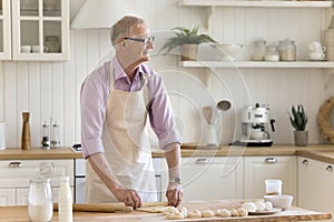 Happy elderly retired man in apron preparing handmade dough for pie