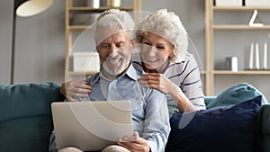 Happy middle-aged couple relax at home using laptop