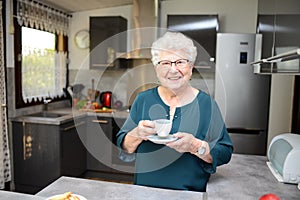 Happy elderly senior active woman drinking coffee in a modern kitchen at home