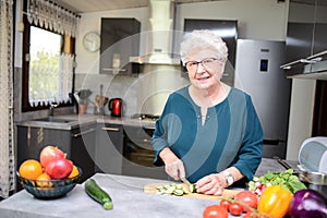 Happy elderly senior old active woman cooking at home in modern kitchen