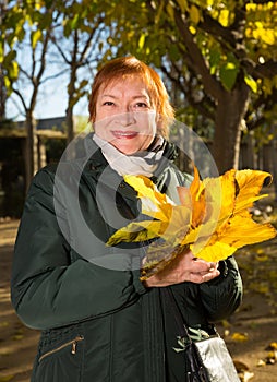 Happy elderly woman with a bouquet of maple leaves in autumn park