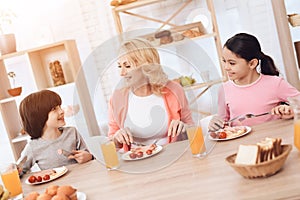 Happy elderly woman dines with her grandchildren at dinner table in kitchen.