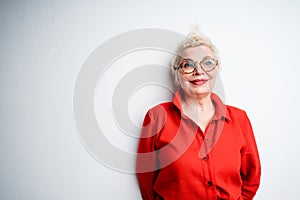 Happy elderly woman with glasses and short hair stands on a light background and smiles photo