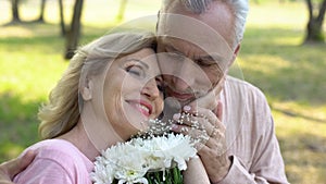 Happy elderly woman holding flowers, stroking male face, mature love, romance
