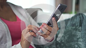 Happy elderly woman holding smartphone in hand, watching screen in home room.