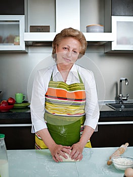 Happy elderly woman in the kitchen holding cooked dumplings and showing thumbs up.