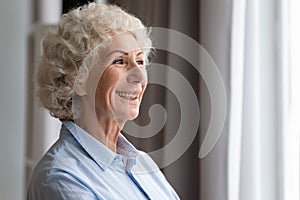 Happy elderly woman looking through window dreaming thinking feeling hope