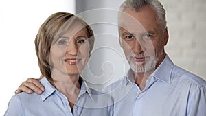 Happy elderly woman and man looking at camera, male hand lying on lady shoulder