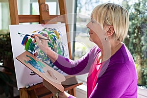 Happy elderly woman painting for fun at home