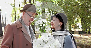 Happy elderly woman plays with bouquet of flowers at her lovely cavalier in park