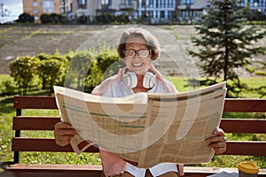 Happy elderly woman reading newspaper in morning in park