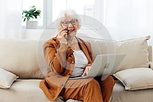 a happy elderly woman smiles sweetly sitting on the sofa in a bright apartment near the window and talking on a