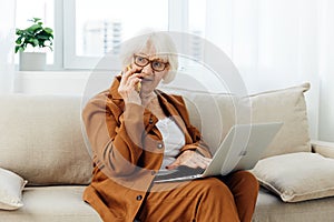 a happy elderly woman smiles sweetly sitting on the sofa in a bright apartment near the window and talking on a