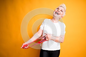 Happy elderly woman in white t-shirt with open mouth stretches elastic band for workouts