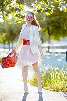 happy elegant female in pink dress and white jacket in city