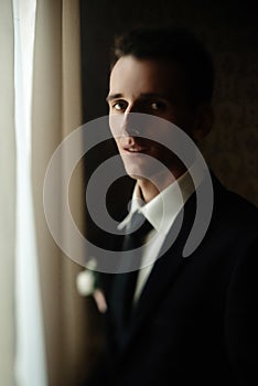 Happy elegant groom getting ready in the morning at window light in rich room