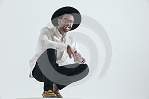 happy elegant man with hat and glasses crouching and smiling