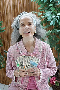 Happy elegant middle-aged woman holding bundles of Dollar banknotes