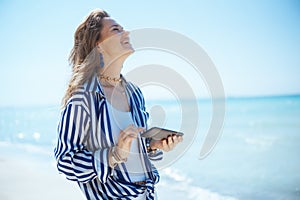 happy elegant woman on seacoast with smartphone