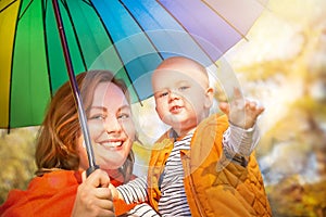 Happy emotional baby boy (child, kid) and mother smiling with colorful umbrella on autumn yellow background.