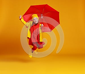 Happy emotional cheerful child girl jumping and laughing  with red umbrella   on colored yellow background