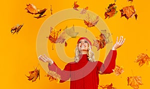 Happy emotional cheerful girl laughing  with autumn leaves and knitted autumn red cap  on colored yellow background