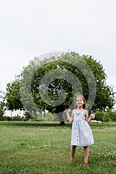 Happy emotional child girl posing outside in the green park. Fashion kid. Smiling toodler girl walking in park.