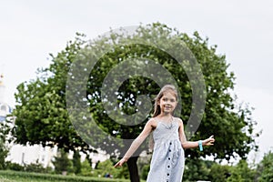 Happy emotional child girl posing outside in the green park. Fashion kid. Smiling toodler girl walking in park.