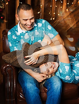 Happy emotional couple have fun together on the couch. The man is sitting. The woman is lying. The husband is trying to strangle a