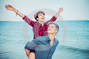 Happy emotional woman with raised up hands on young man`s back. Couple enjoying each other, having fun on the beach. Date, love s