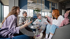 Happy emotional young students spending free time in campus, playing exciting board card game