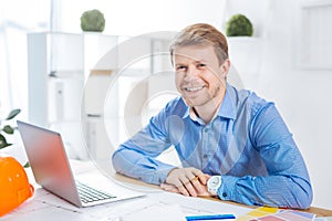 Pleasant man smiling and sitting opposite the laptop