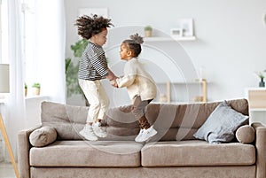 Happy energetic african american children jumping on sofa