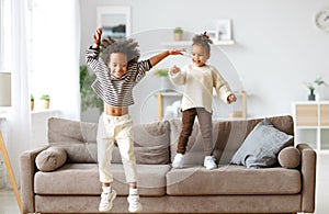 Happy energetic african american children jumping on sofa