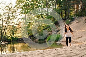 Happy little girl running on sandy beach close to river. Junior active athlete doing sports and having fun near water.