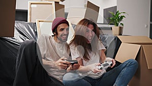A happy and engaged couple, a brunette girl and her boyfriend with stubble in a beige T-shirt play video games using two
