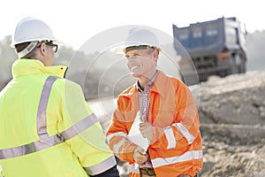 Happy engineer discussing with colleague at construction site on sunny day