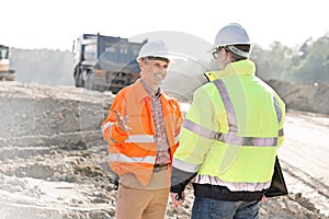 Happy engineer talking to colleague at construction site on sunny day
