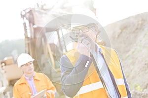 Happy engineer using walkie-talkie on construction site with colleague in background