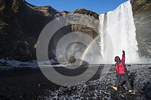 Happy and enjoy road trip with hand up at big Skogafoss waterfall Iceland and double rainbow in sunnyday in winter. photo