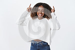 Happy enthusiastic and carefree attractive young african-american woman with curly hair in winter white trendy sweater