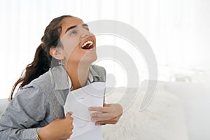 Happy entrepreneur woman reading good news in a letter on sofa in home