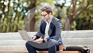 Happy entrepreneur working with laptop computer while sitting on stairs in urban park