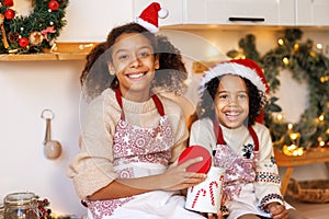 Happy ethnic children on Christmas eve,   girl and boy eat cookies that they baked together in cozy kitchen at home