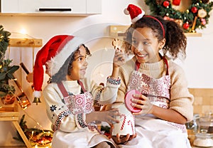 Happy ethnic children on Christmas eve,   girl and boy eat cookies that they baked together in cozy kitchen at home