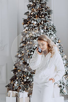 happy european businesswoman talking on mobile phone with client at workplace with decorated Christmas tree behind, smiling woman