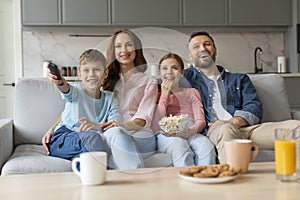 Happy european family with their preteen kids watching tv together at home